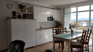 A modern kitchen with white cabinets, a dining area with wooden chairs, and a large window offering a view of the countryside. - Living Home (Sibiu)