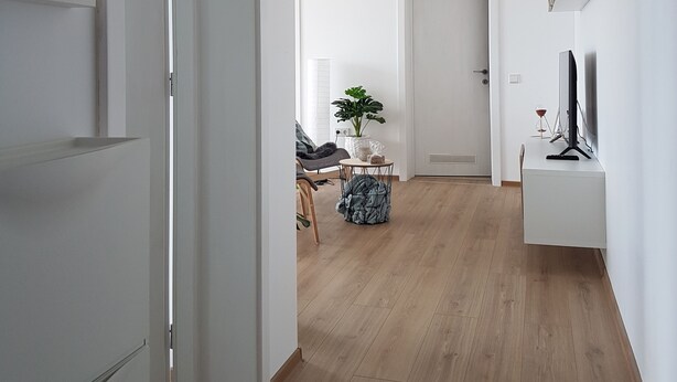 A modern, minimalist living space with a wooden floor, white walls, and a central area with a round table and a potted plant. - Living Home (Sibiu)
