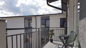 A balcony with a small table and two chairs, a potted plant, and a view of a building with windows. - Living Home (Sibiu)