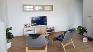 A modern living room with a flat-screen TV, two grey chairs with fur throws, a white console table, and a wooden cabinet with glass doors. - Living Home (Sibiu)