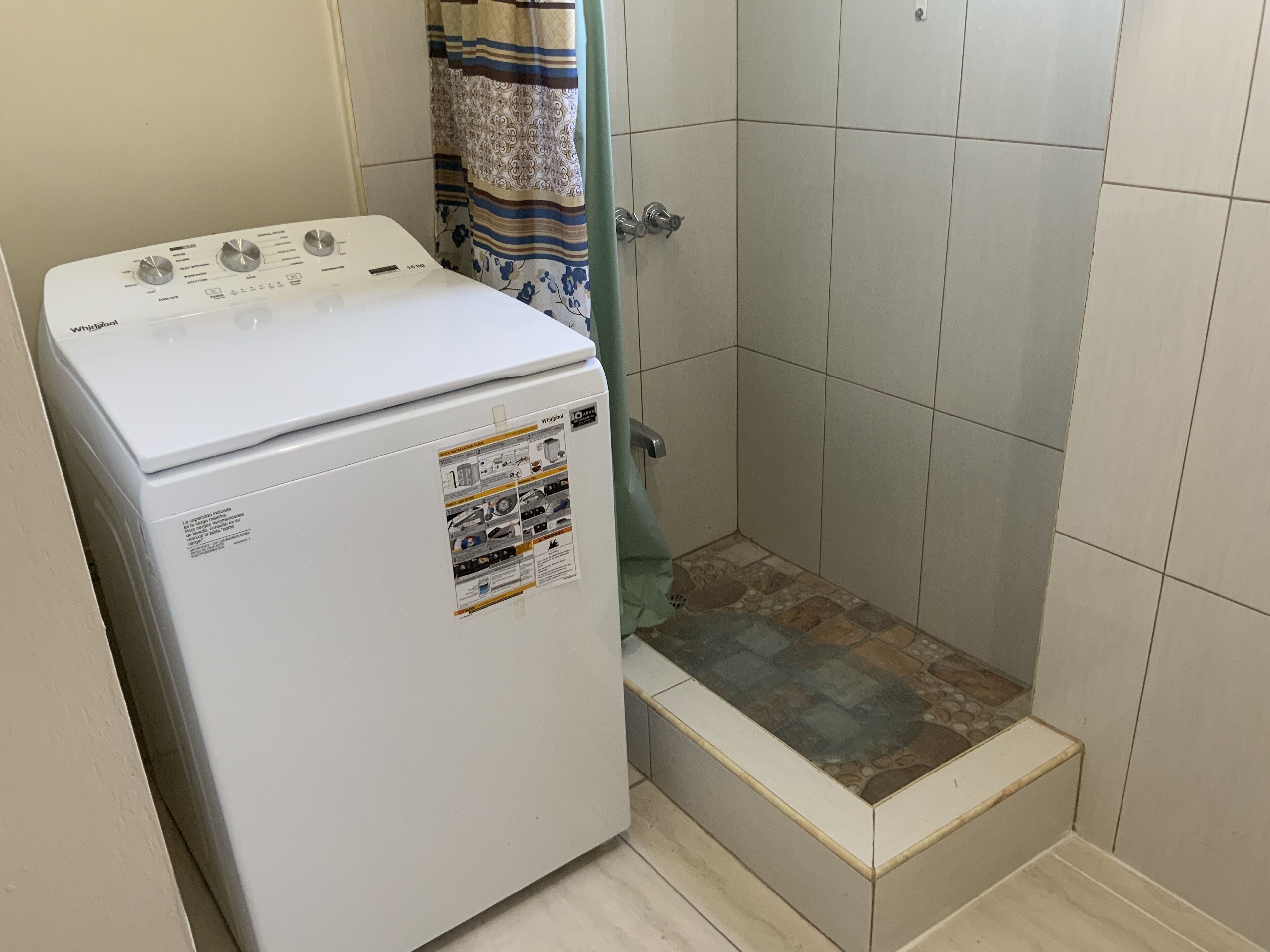 Eine kompakte Waschmaschine und ein Trockner in einem kleinen Badezimmer mit gefliesten Wänden und einer Duschkabine.