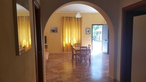 Un coin repas avec une table et des chaises, un tableau accroché au mur et une vue sur l’extérieur par une porte.