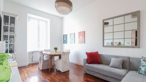 A modern living room with a dining area, a grey sofa with red and grey cushions, a large mirror, and three framed pictures on the wall. - Near Vatican Museums Rome (Roma)