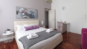 A neatly arranged bedroom with a large bed, a bedside table with a lamp, a small round side table with a plant, and a wall-mounted painting. - Near Vatican Museums Rome (Roma)