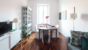 A modern living room with a wooden dining table, white chairs, a sofa, a TV, and a cabinet. - Near Vatican Museums Rome (Roma)