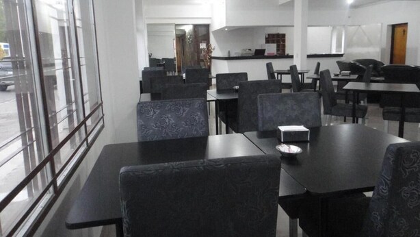 A modern dining area with black tables and chairs, a kitchen in the background, and large windows. - HOTEL LOS ANTIGUOS (Los Antiguos)
