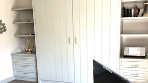 Una habitación con un armario amplio, un televisor de pantalla plana sobre un soporte blanco, y piso de madera.