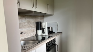 Una cocina compacta con armarios blancos, un lavamanos de acero inoxidable, una cafetera y un horno negro.