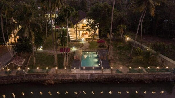 A two-story house with a swimming pool, surrounded by palm trees and a body of water. - Lhasa Ayurveda and Wellness Resort (North Paravur)