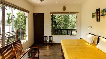 A hotel room with a bed, a table, two chairs, a ceiling fan, and large windows with a view of palm trees.