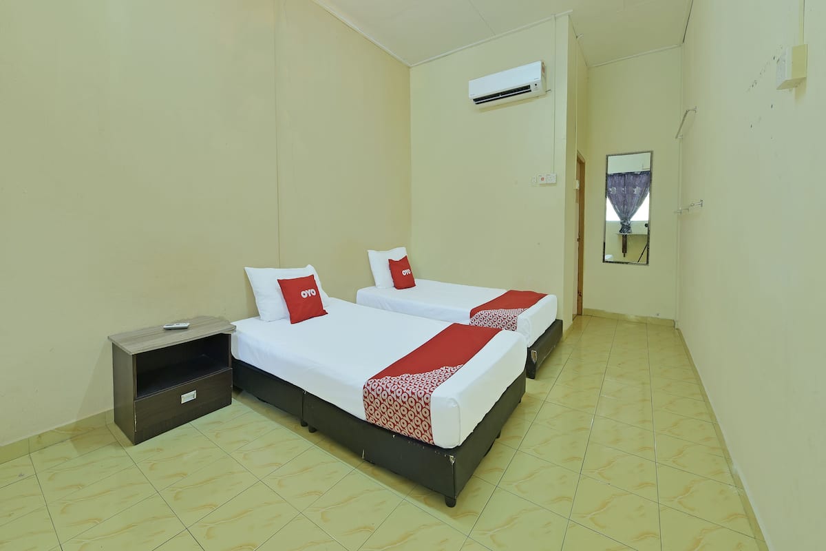A small hotel room with two beds, a nightstand, a mirror, and an air conditioning unit.