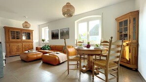 A spacious living room with a large sofa, a dining table with chairs, and a kitchen area with wooden cabinets.