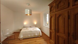 A bedroom with a bed, bedside lamps, a wooden wardrobe, and a window.