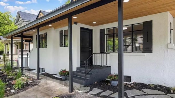 Ein modernes Haus mit einer überdachten Veranda, einer Haustür und einer Treppe, die zum Eingang führt.