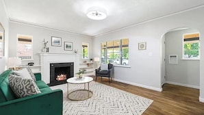 Ein Wohnzimmer mit Kamin, grünem Sofa und Blick ins Freie durch große Fenster.