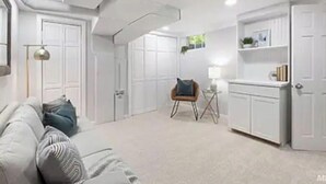 Ein moderner, gut beleuchteter Raum mit einer Couch, einem Sessel, einem kleinen Tisch und einem Schrank.