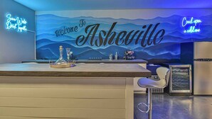 Un espace d’accueil avec une pancarte « Bienvenue à Asheville », un panneau lumineux et un bar équipé d’un shaker à cocktails.