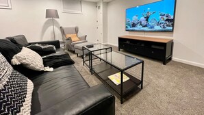 Un salon moderne avec un canapé en cuir noir, une table basse en verre, un téléviseur fixé au mur et une lampe.