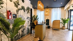 A reception area with a reception desk, a black office chair, a wicker chair, and potted plants. - Maison Paradis Marseille (Marseille)