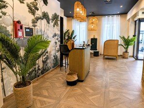 A reception area with a reception desk, a black office chair, a wicker chair, and potted plants. - Maison Paradis Marseille (Marseille)