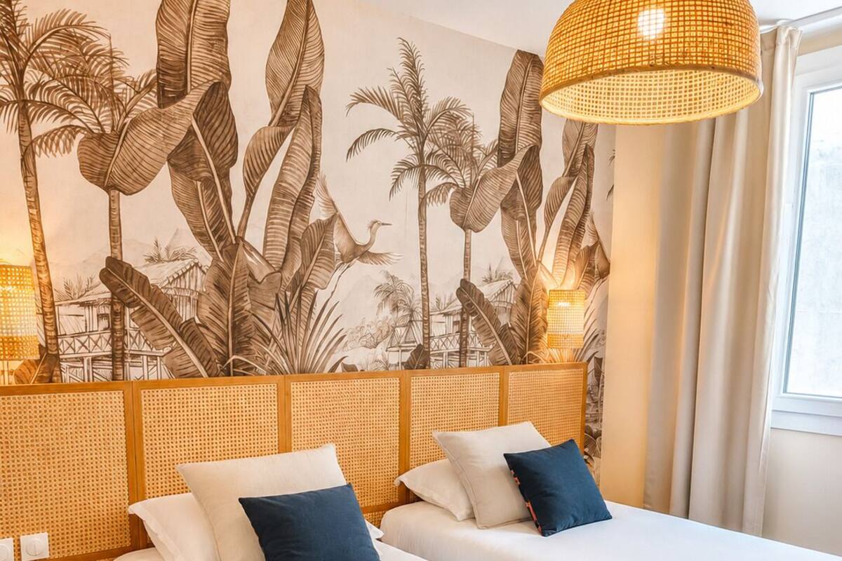 A hotel room with two beds, a woven headboard, a rattan lamp, and a tropical mural.