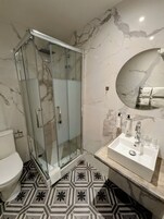 A bathroom with a glass-enclosed shower, a white sink with a mirror, and patterned floor tiles.