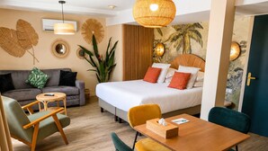 A hotel room with a bed, sofa, dining table, chairs, and a plant. - Maison Paradis Marseille (Marseille)