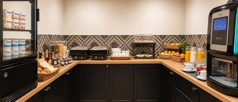 A modern kitchen with a coffee machine, breakfast items, and a fruit basket.