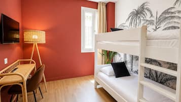 Une chambre avec un lit superposé, un bureau avec une chaise, une lampe et un mur orné d’une fresque aux motifs tropicaux.