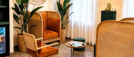 A modern living room with a sofa, armchairs, a coffee table, and a bed. There are wicker lamps, a mirror, and potted plants.