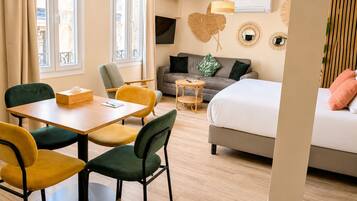 Een moderne hotelkamer met een bed, een bank, een eettafel met stoelen, een televisie en een groot raam.
