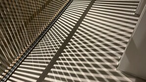 A staircase with a geometric pattern of shadows cast by vertical blinds.