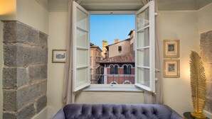 Una habitación con un ventanal grande, paredes de piedra, un sofá capitonado y cuadros enmarcados.