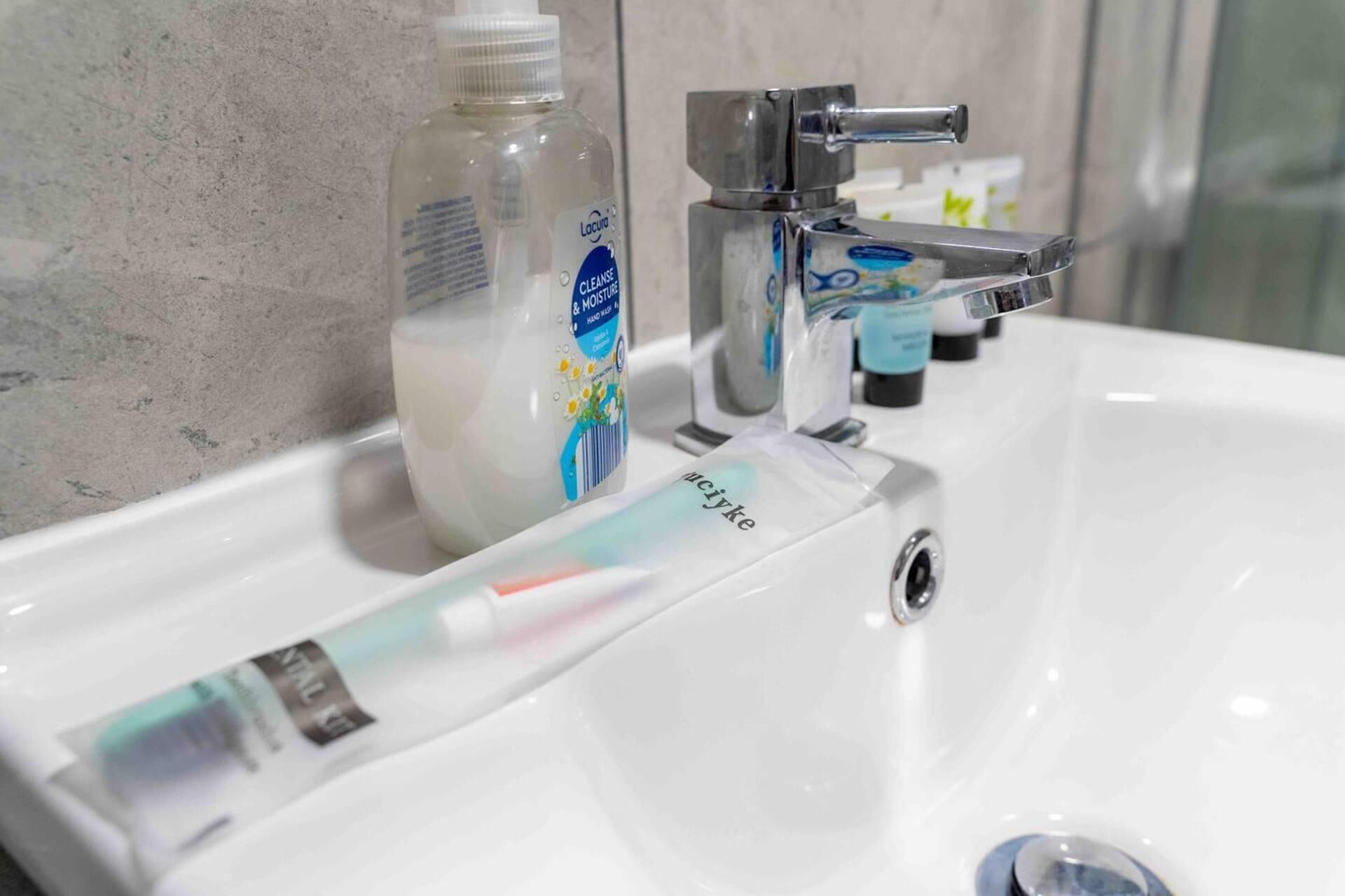 A bathroom sink with a bottle of liquid soap, a faucet, and a tube of toothpaste.