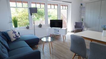Un salon moderne comprenant un canapé, une table basse en verre, un téléviseur à écran plat et un coin repas avec une chaise et une table.