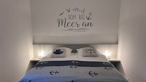 Ein ordentlich bezogenes Bett mit einem Bezug und Kissen im Seestil, eine Wand mit einer maritimen Dekoration und Nachttischlampen.