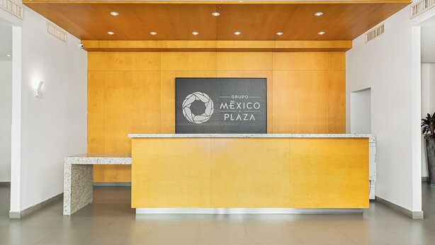 Un mostrador de recepción con un revestimiento de pared de madera y el logotipo de Grupo Mexico Plaza.