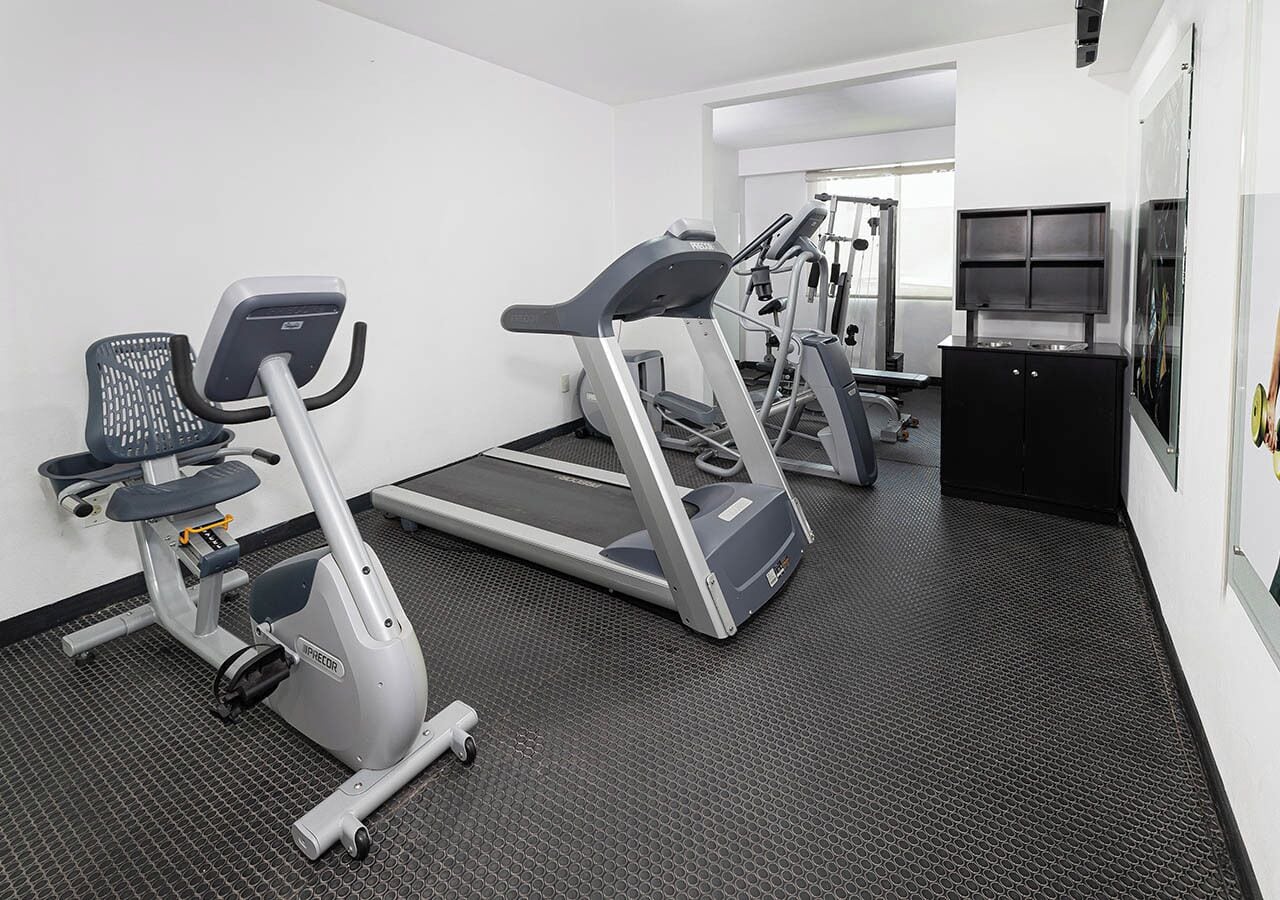 A gym with treadmills and elliptical machines, a black cabinet, and a door leading to another room.