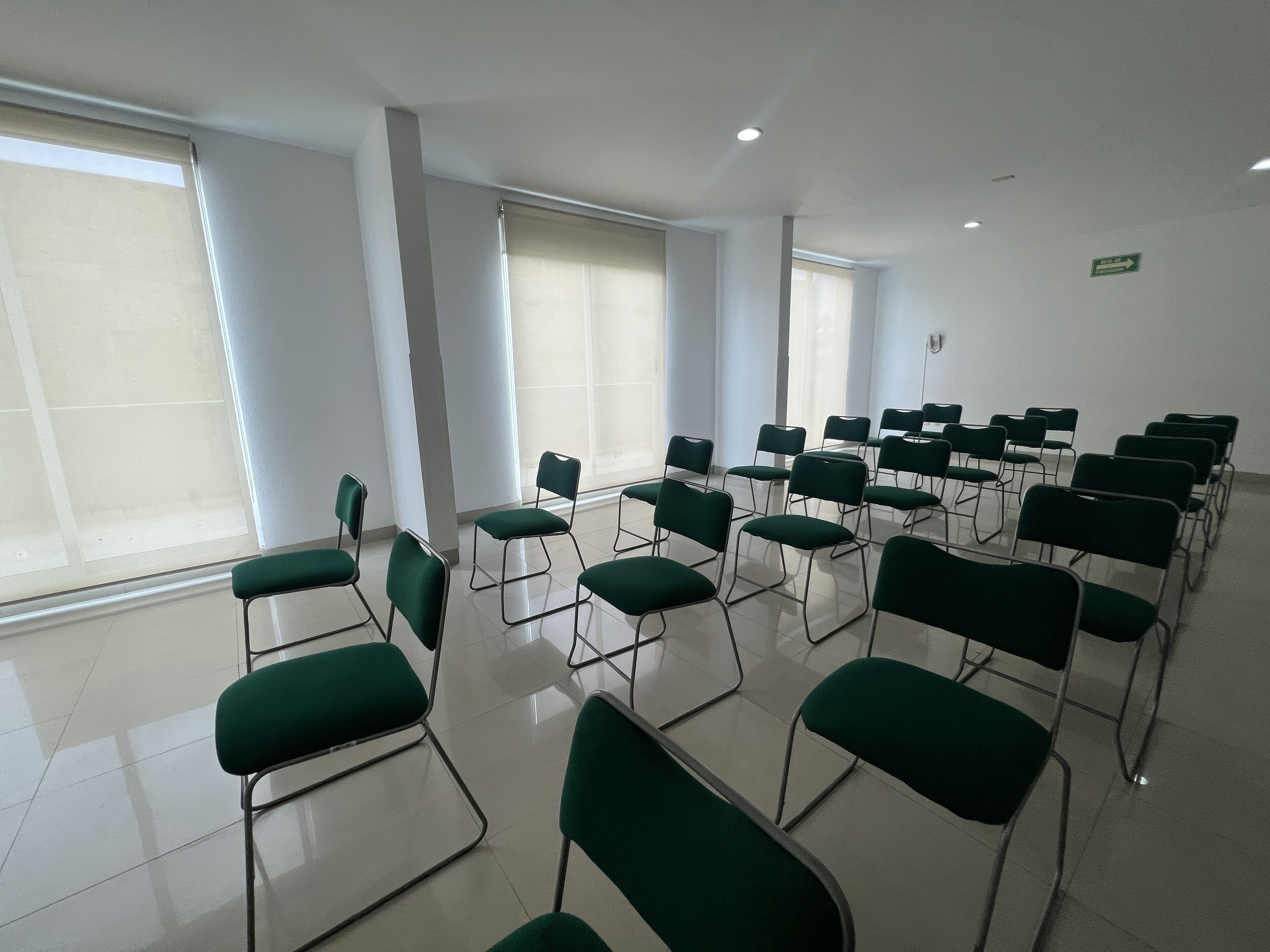A conference room with rows of green chairs, large windows, and a clean, tiled floor.