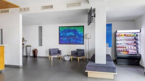 Un vestíbulo moderno con zona de estar, un cuadro abstracto de gran tamaño, una máquina expendedora y un televisor de pantalla plana.