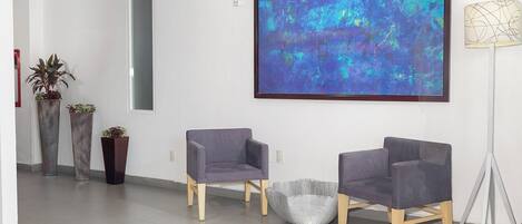 A modern waiting area with two grey chairs, a floor lamp, and a large abstract painting on the wall.
