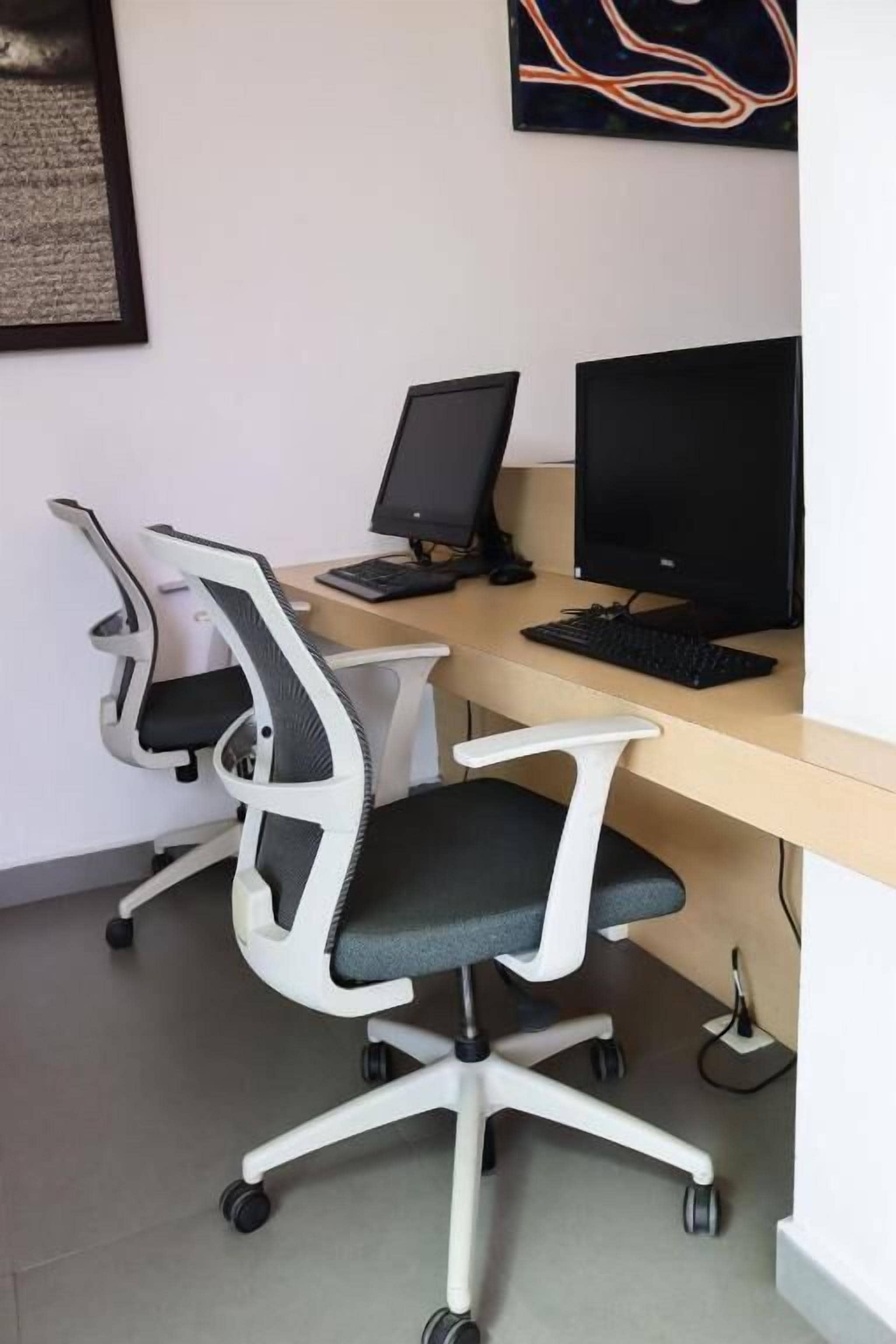 Un espace de travail comprenant deux chaises de bureau, un bureau, deux écrans et un clavier.
