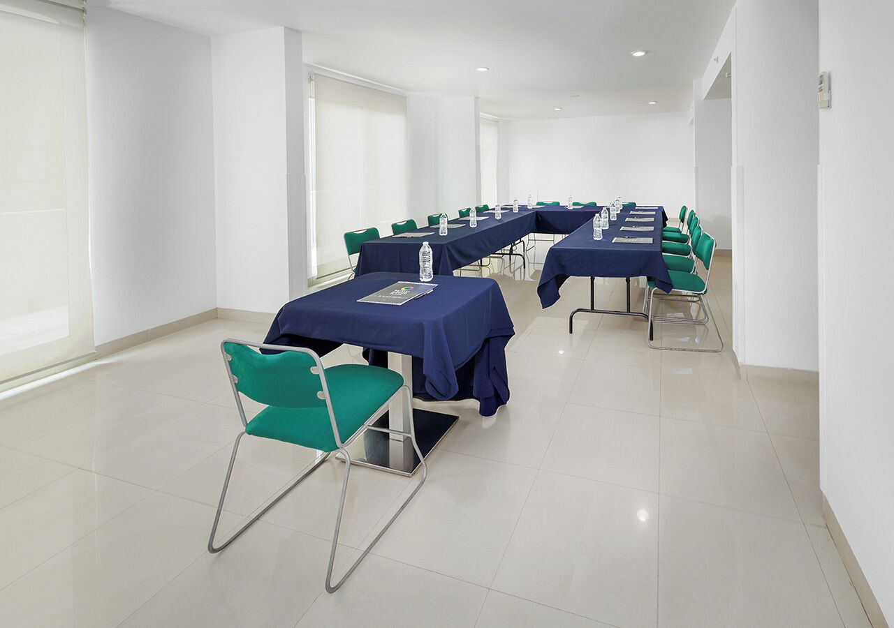 Une salle de conférence équipée de tables et de chaises, de grandes fenêtres et d’un sol carrelé.