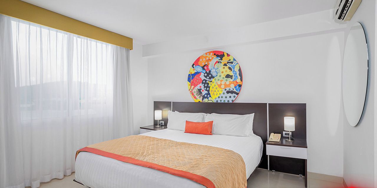 Een hotelkamer met een bed, twee nachtkastjes, een groot rond schilderij en een bord met 'BLACK FRIDAY'.
