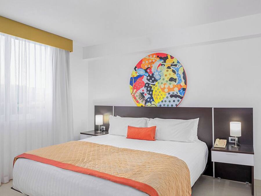 Een hotelkamer met een bed, twee nachtkastjes, een groot rond schilderij en een bord met 'BLACK FRIDAY'.