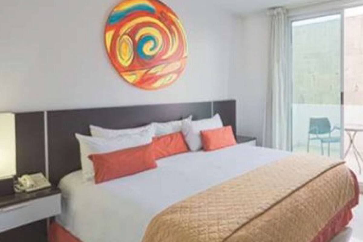 Habitación de hotel con una cama grande, una mesita de noche, un teléfono y una obra de arte colorida en la pared.
