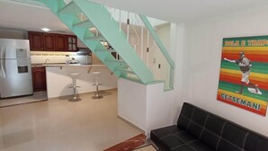 A modern kitchen with a stainless steel refrigerator, wooden cabinets, and a teal staircase leading to an upper level. - Beautiful small house close Getsemani (Cartagena de Indias)