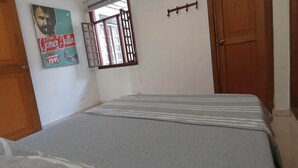 A bedroom with a bed, a window with a metal grill, a wooden door, and a wall with a poster. - Beautiful small house close Getsemani (Cartagena de Indias)