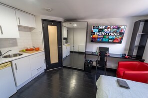 A modern kitchen with white cabinets, a black door, and a flat-screen TV displaying a movie selection. - Lovely Studio Close to University of Birmingham! (Birmingham)