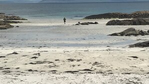 A beach with a person walking towards the water, rocky outcrops, and a distant island. - Luxury safari tent, outdoor bath sleeps 6. Near to Aran Island ferries and beach (Ballynahown South)